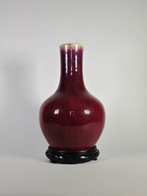 un vase rouge posé sur un socle noir, lui-même posé sur une surface blanche