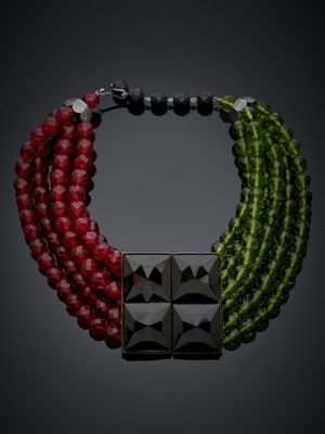 un gros plan d'un collier sur fond noir, orné de perles rouges et vertes