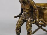 bronze figurine of a man pulling a cart with a cow