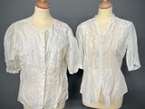 two mannequins with white blouses on display against a gray background