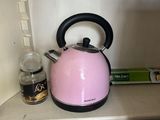 a pink tea kettle sitting on a shelf in a cupboard