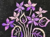 purple flowers are embroidered onto a black velvet bag on a table
