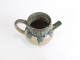 une petite tasse avec une anse posée sur une surface blanche