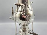 an antique silver plated coffee urn with a handle and legs
