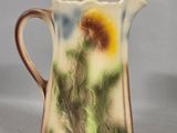 a small pitcher with a flower on it on a table