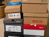 Plusieurs cartons de chaussures sont empilés sur une table, à côté d'une plante en pot.