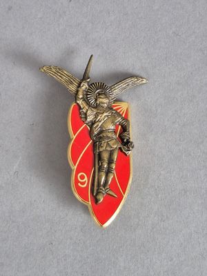 une photo d'une broche rouge et dorée représentant un ange tenant une épée