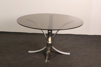 une table en verre avec un piètement en métal, posée sur un sol recouvert de moquette