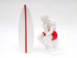 figurine of a man sitting next to a surfboard on a white surface