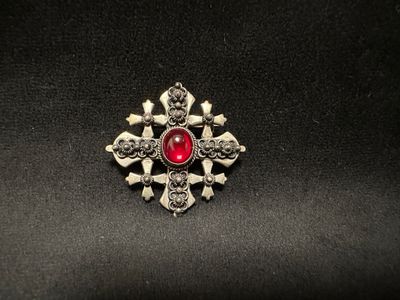 a close up of a broochle with skulls and a red stone