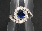 une photo d'une bague sertie d'un saphir bleu et de diamants, posée sur un présentoir transparent