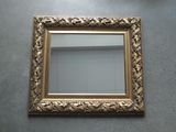gold framed mirror on the floor with a white wall in the background