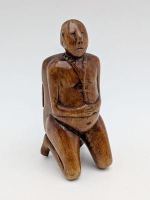 an old wooden figurine of a man sitting on a stool