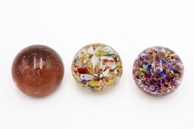 trois perles de verre de couleurs différentes posées les unes à côté des autres sur une surface blanche