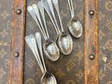 six cuillères en argent posées sur une vieille valise posée sur une table