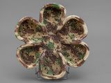a small ceramic flower on a stand on a gray surface
