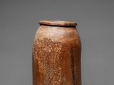 an old brown jar with a lid sitting on a gray surface