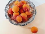 a bowl of apricots sitting on a table next to two oranges