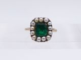 a close up of a ring with pearls and an emerald