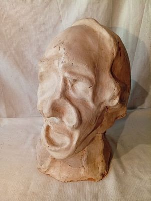 une sculpture en argile représentant le visage d'un homme, posée sur un tissu blanc