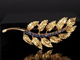 un gros plan sur une broche en feuille d'or sertie de pierres bleues