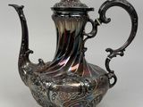 silver plated tea pot with ornate design on stand