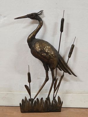 a bronze statue of a crane standing on a pond