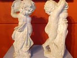 pair of white marble statues of angels on a table in front of a painting