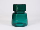 un bocal en verre vert avec un couvercle vert posé sur une surface blanche