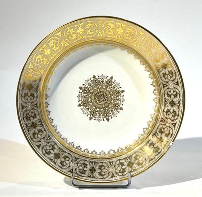une assiette dorée et blanche posée sur un support, sur une surface blanche