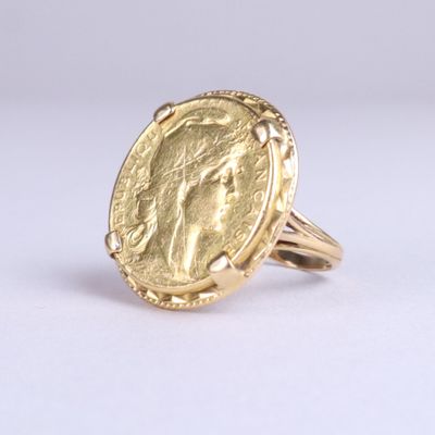un gros plan d'une bague en forme de pièce d'or posée sur une surface blanche