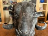 statue représentant une tête de bélier posée sur une table en bois devant une bibliothèque