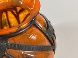 an orange and black vase sitting on a white surface