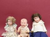 trois poupées en porcelaine assises les unes à côté des autres sur une surface rouge