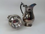 a silver pitcher next to a silver cup on a table