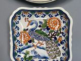 two plates with peacocks and flowers on them sitting next to each other