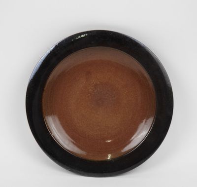 une assiette marron et noire posée sur une surface blanche, avec un fond blanc