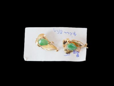 une paire de boucles d'oreilles dorées et vertes posées sur un morceau de papier