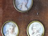 three miniature portraits of women are displayed on a wooden surface