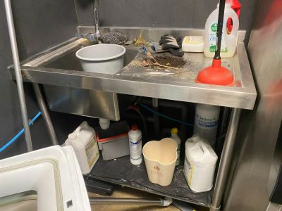 a sink in the corner of a kitchen with a lot of clutter on the floor