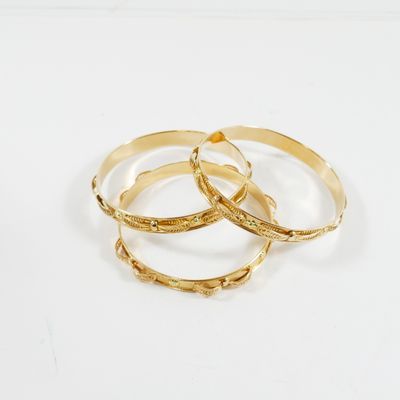 un ensemble de trois bracelets rigides dorés sur fond blanc