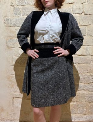 a woman standing in front of a wall wearing a skirt and jacket