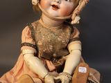 an old fashioned doll sitting on the ground wearing a bonnet and dress