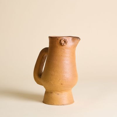 un petit pichet marron posé sur une surface blanche
