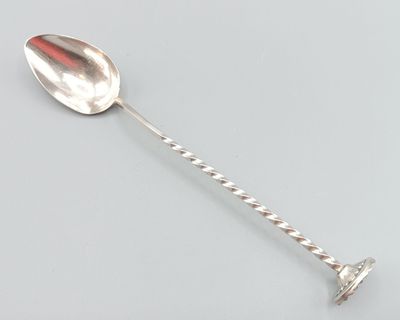 une cuillère en argent au manche torsadé posée sur une surface grise