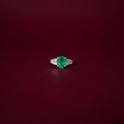 an emerald and diamond ring on a red surface