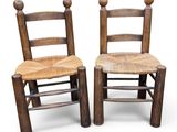 pair of wooden chairs with rope seat and backrests against a white background