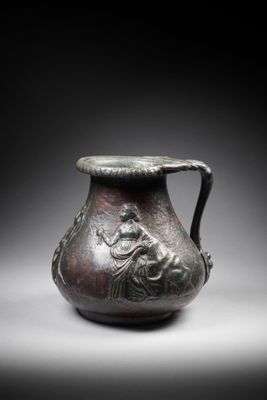 une vieille cruche en bronze munie d'une anse, posée sur une surface blanche