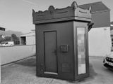 photographie en noir et blanc d'une petite cabine téléphonique publique située dans un parking