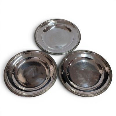 three silver metal plates sitting on top of each other on a white surface